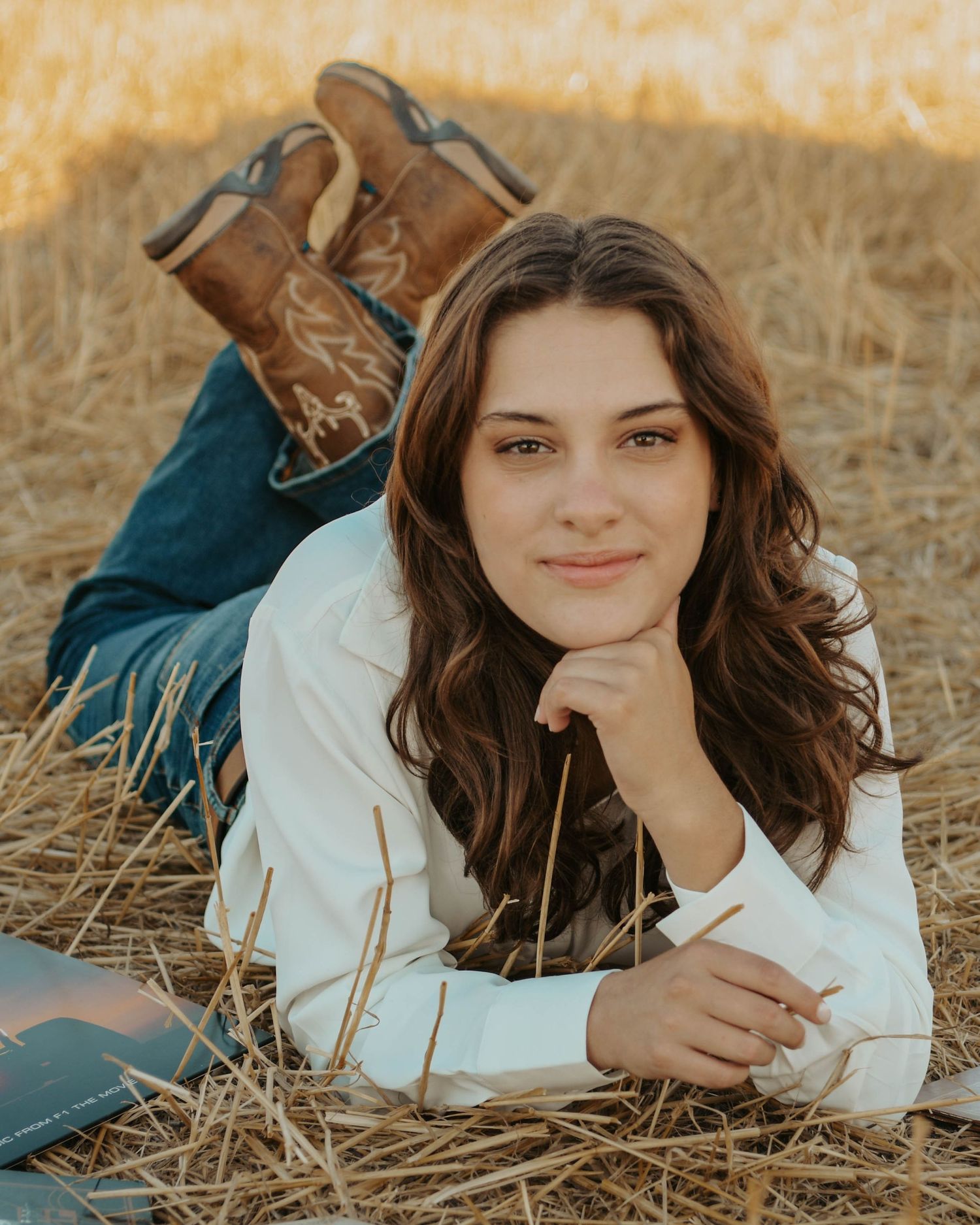 Person lying in golden wheat field wearing white sweater and brown boots during outdoor portrait session.