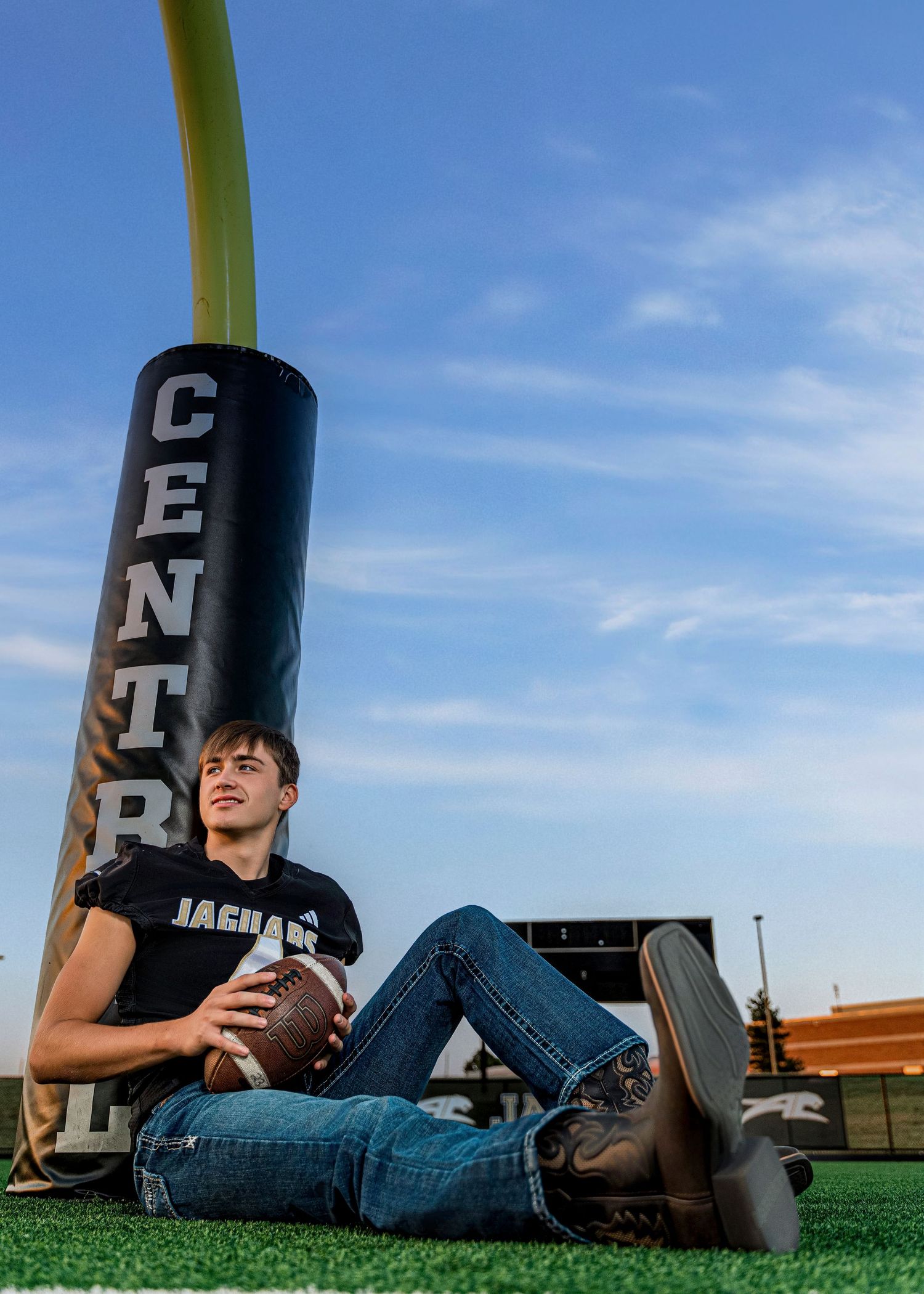 High school athlete posing with football training equipment on a sunny field.