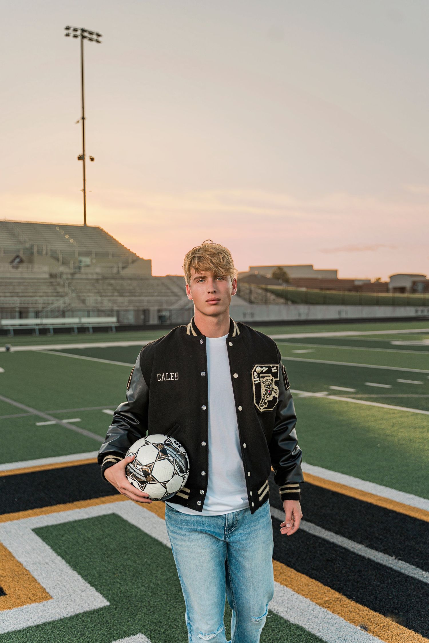 Varsity letterman jacket and jeans outfit shown in four similar poses on a football field at sunset.