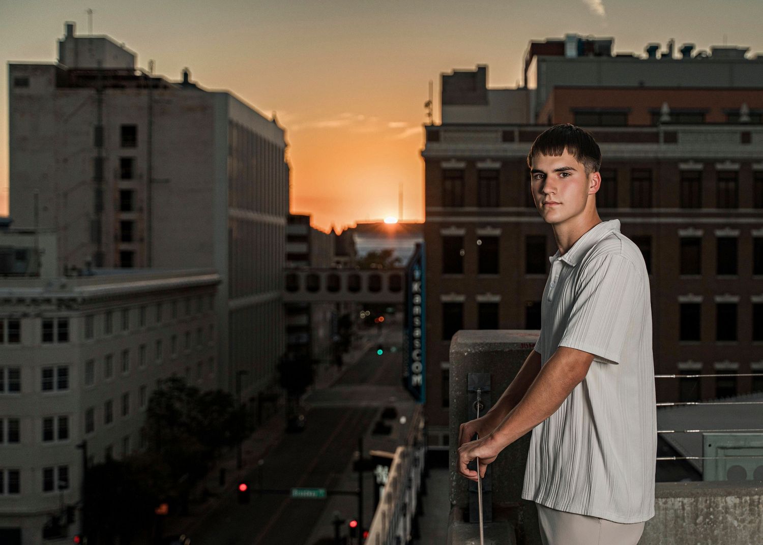 Person in white shirt stands on urban rooftop against dramatic orange sunset sky in city setting.