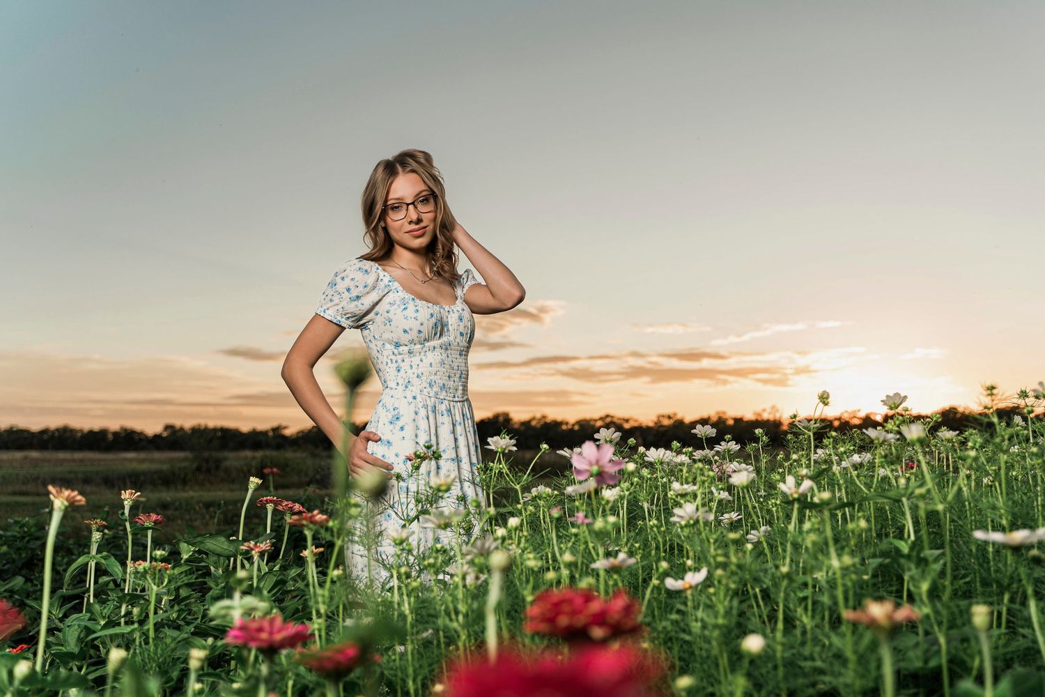 A person in a floral dress stands in a wildflower field with poppies during golden sunset hour.