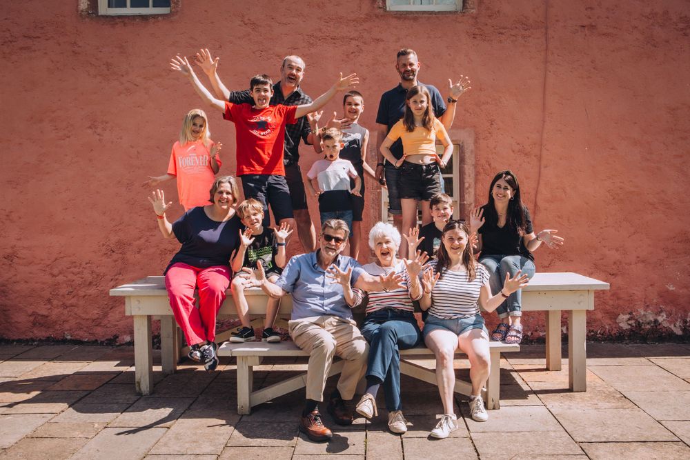 A cheerful group poses together on wooden benches against a red brick wall outdoors.