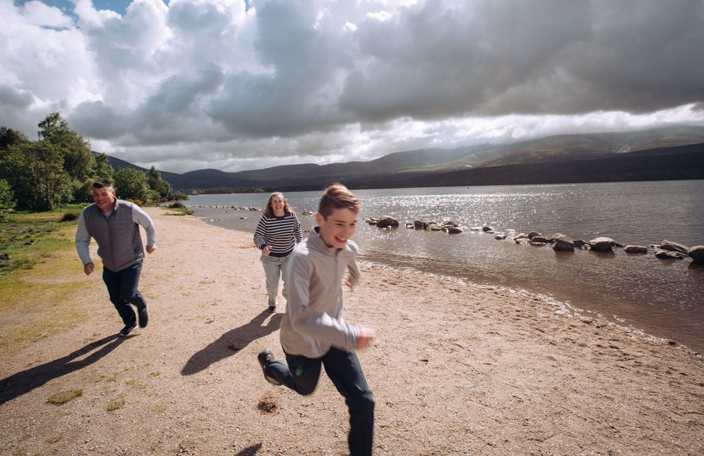 People running along a scenic beach path with moody storm clouds over a lake and mountains in the background.