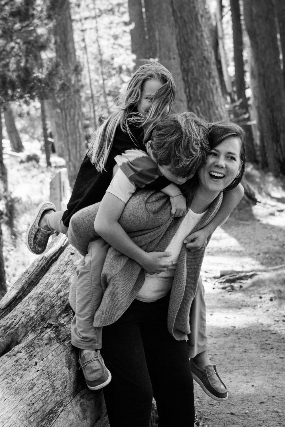 A joyful black and white moment captured on a forest path as people share playful piggyback rides and laughter.