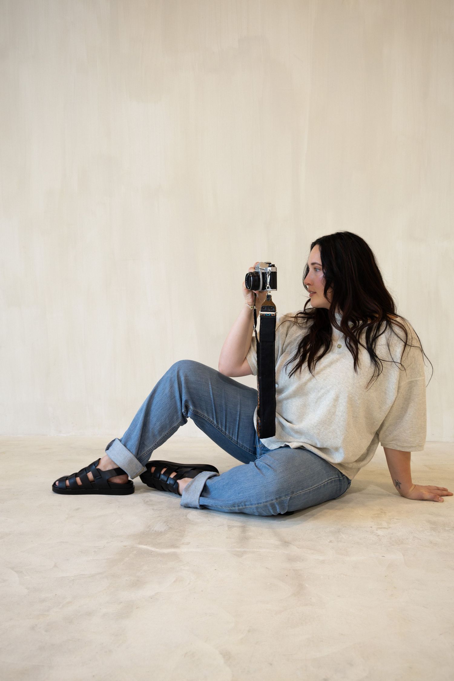 Person in casual attire lying on a beige floor in a minimalist setting while using a film camera.