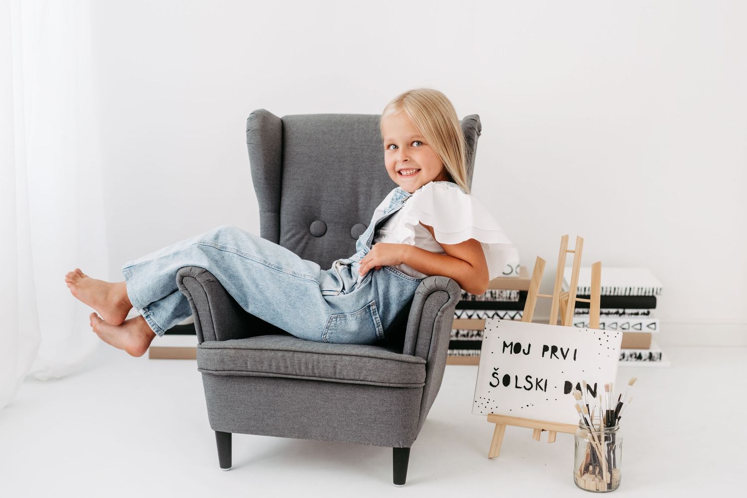 Young artist relaxing in grey wingback chair beside miniature easel display.