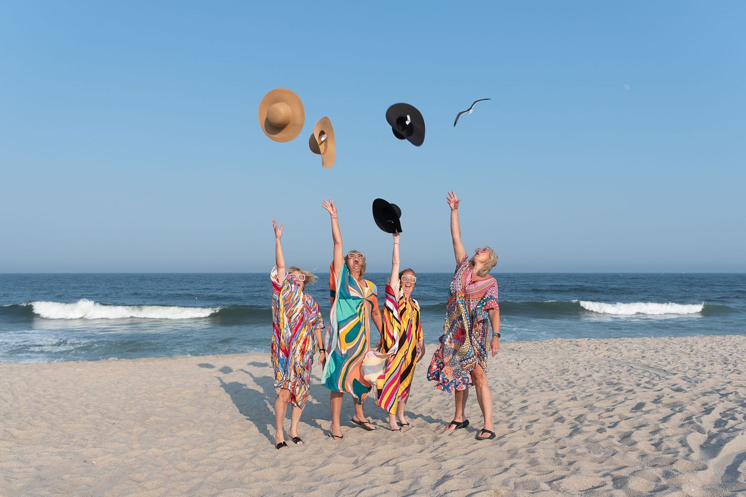 Group of graduates celebrating on beach by throwing caps in air.