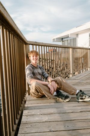 Person sitting on wooden deck with railing overlooking scenic view.