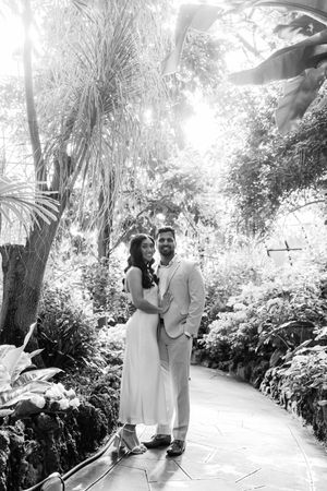 A romantic couple shares tender moments in a lush garden setting captured in black and white photography.