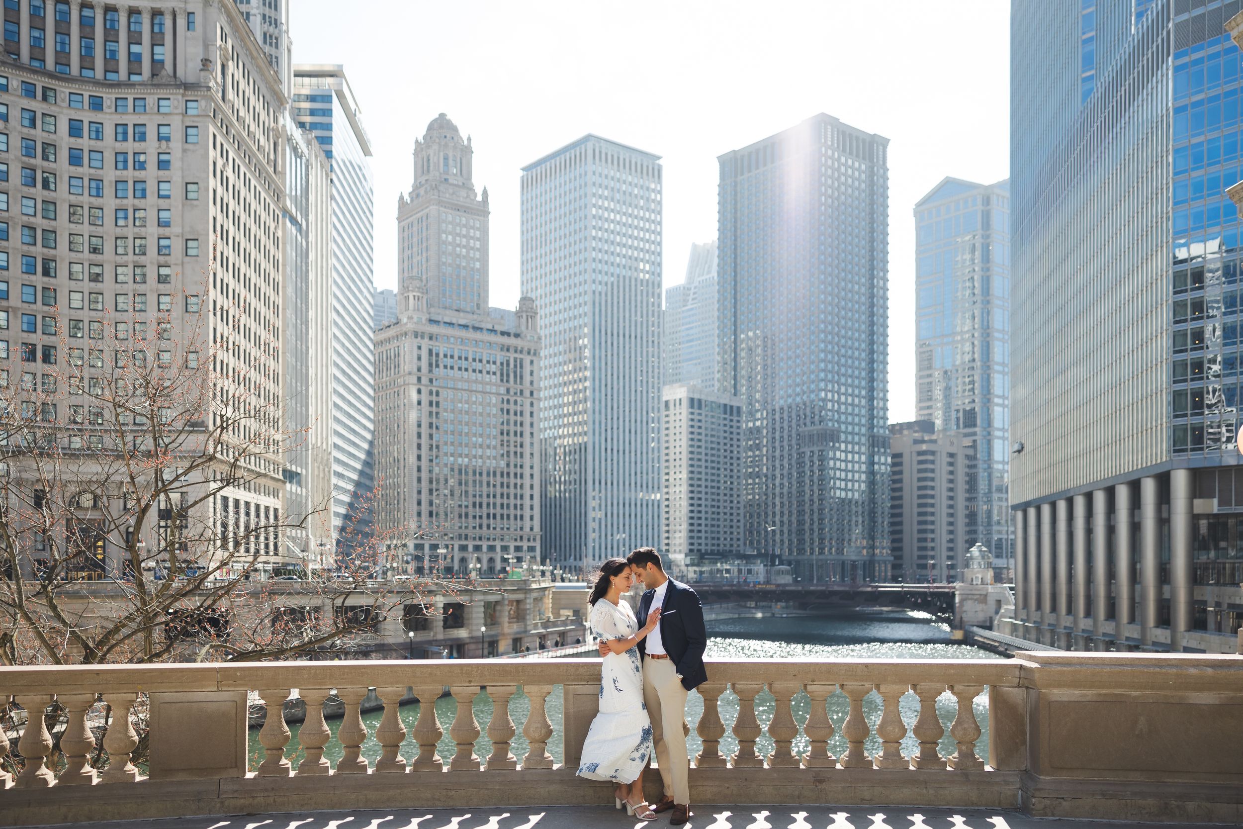 A couple shares a romantic moment on a balcony overlooking the Chicago River with iconic skyscrapers in the background.