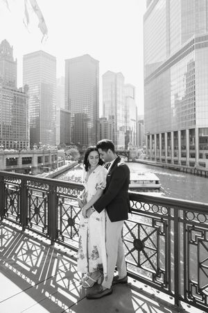 Couple shares romantic moment along ornate railing of Chicago River with city skyline in background.