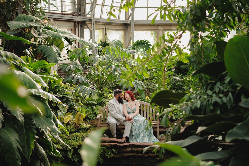 Lush greenhouse interior with abundant tropical plants and seating areas beneath a glass dome ceiling.
