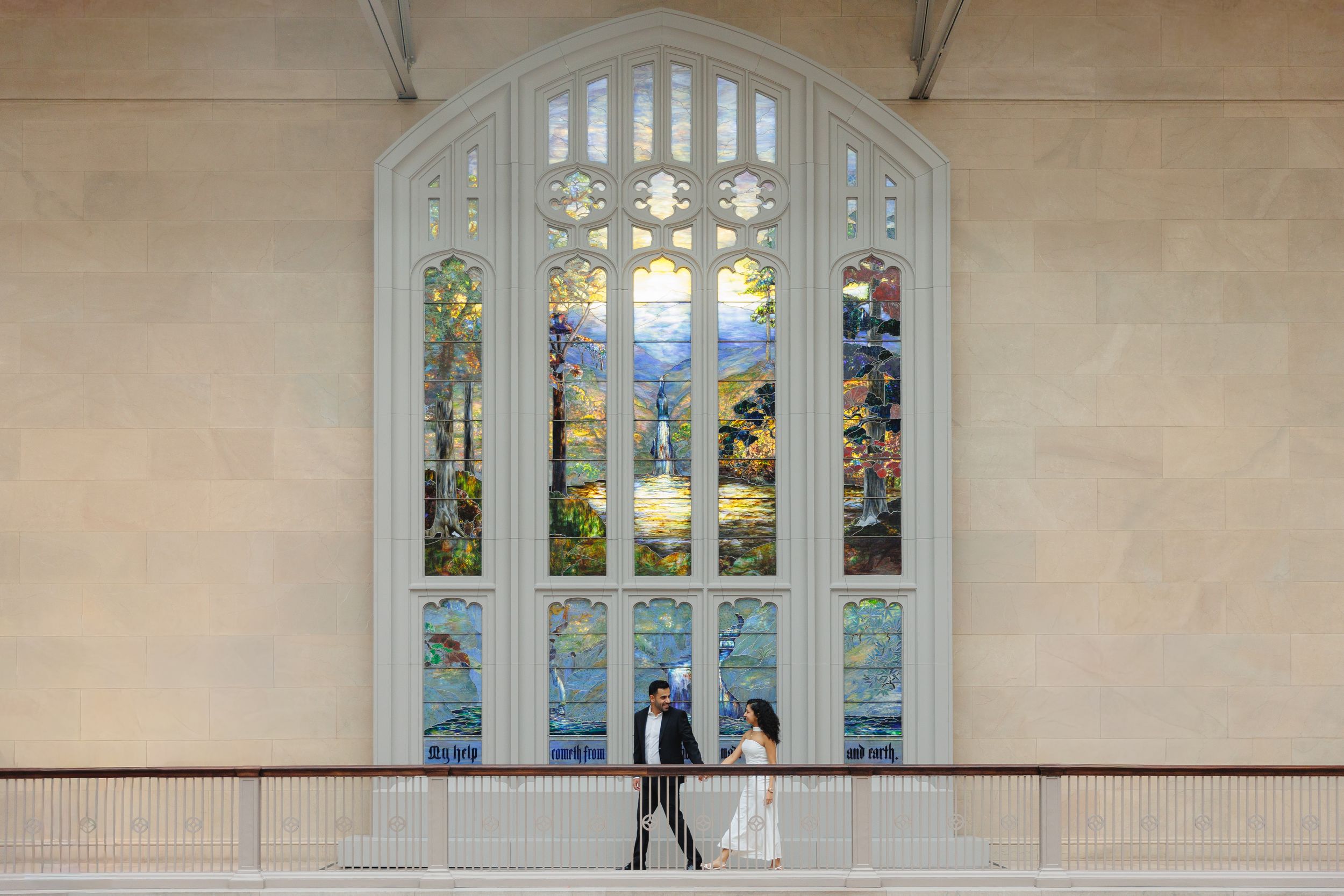 Arched stained glass windows line a beige wall in an elegant interior hallway.