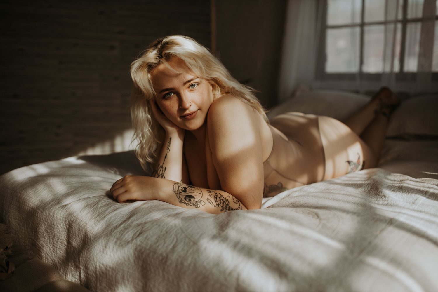 Intimate natural light portrait on white bedding with soft window lighting.