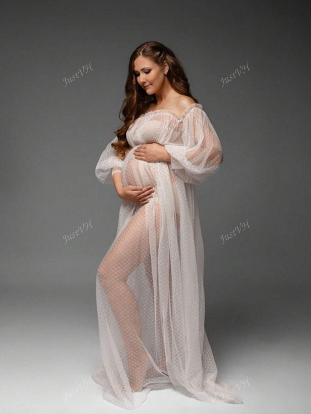Elegant maternity photo featuring a flowing sheer white lace dress with puff sleeves against a dark gray studio backdrop.