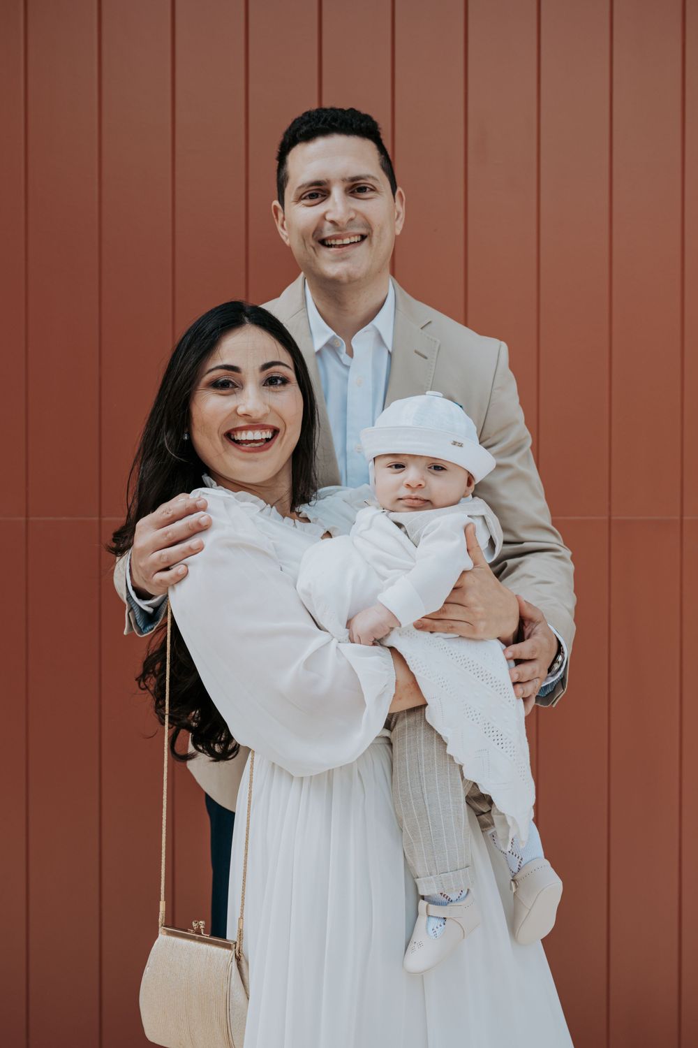 A family wearing white and beige poses together against a brown wall during a special occasion.