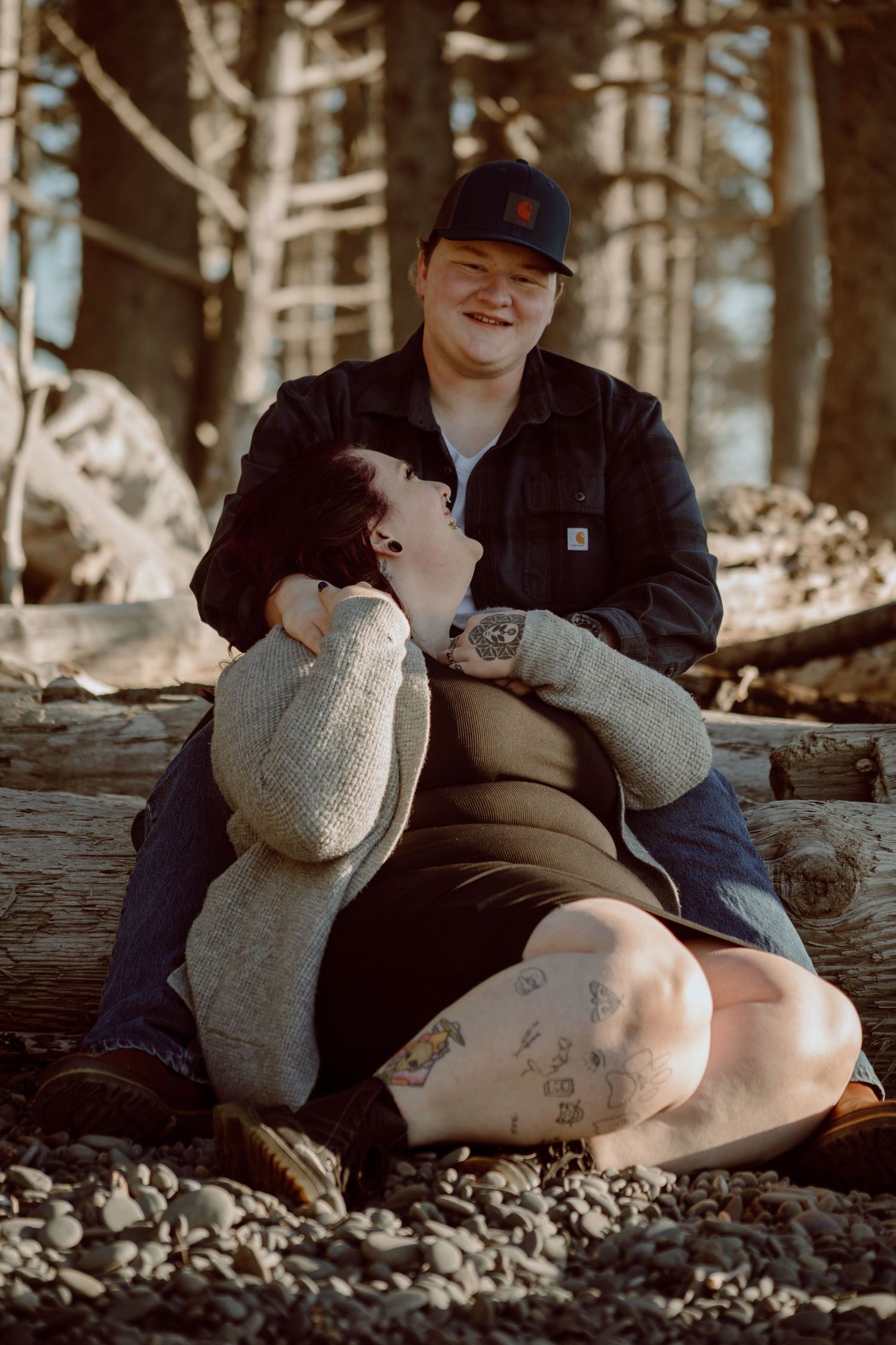 Two people sharing intimate moment while sitting on driftwood at rocky beach.