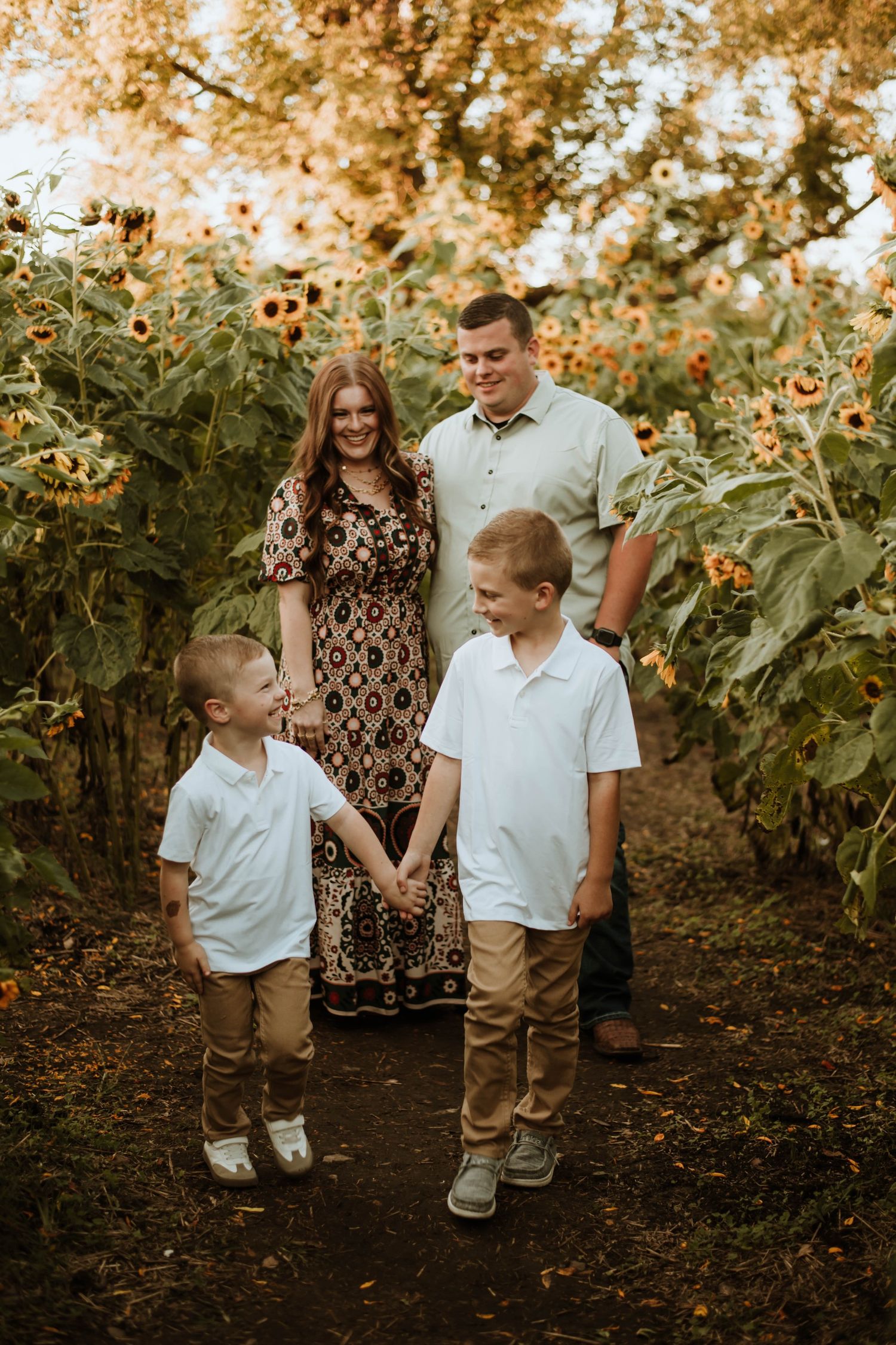 Family walking through a sunflower field during golden hour with warm autumn lighting.