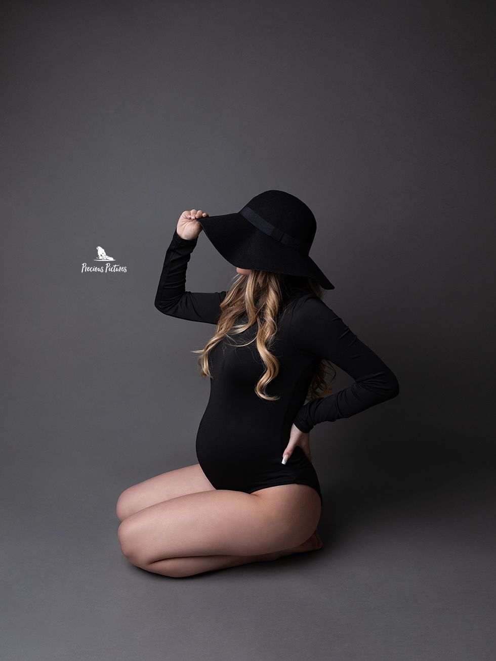 High-fashion studio maternity portrait in a black bodysuit and wide-brimmed hat, artistic pregnancy photography by Precious Pictures, Malta.