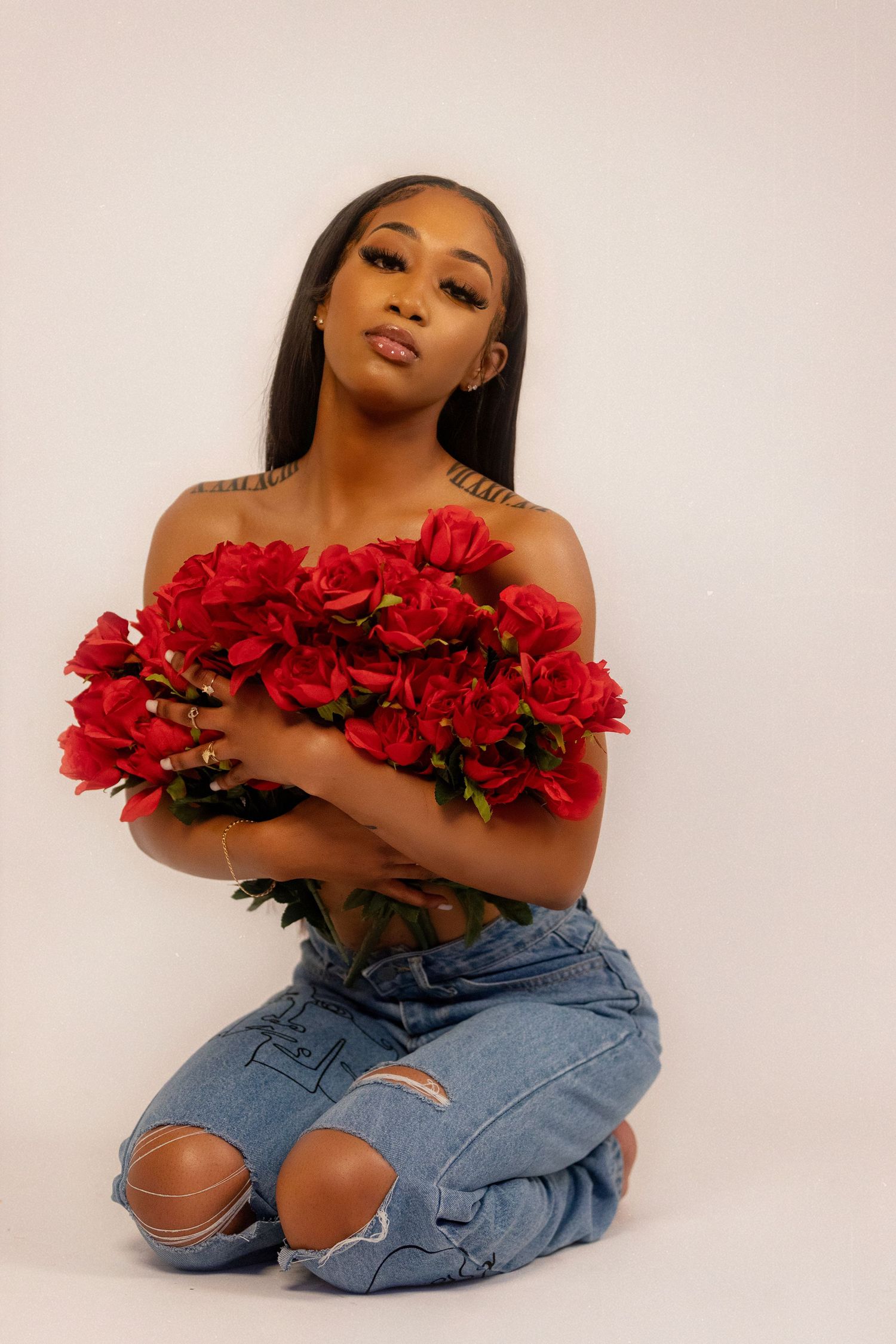 Portrait with red roses against light background wearing distressed denim.