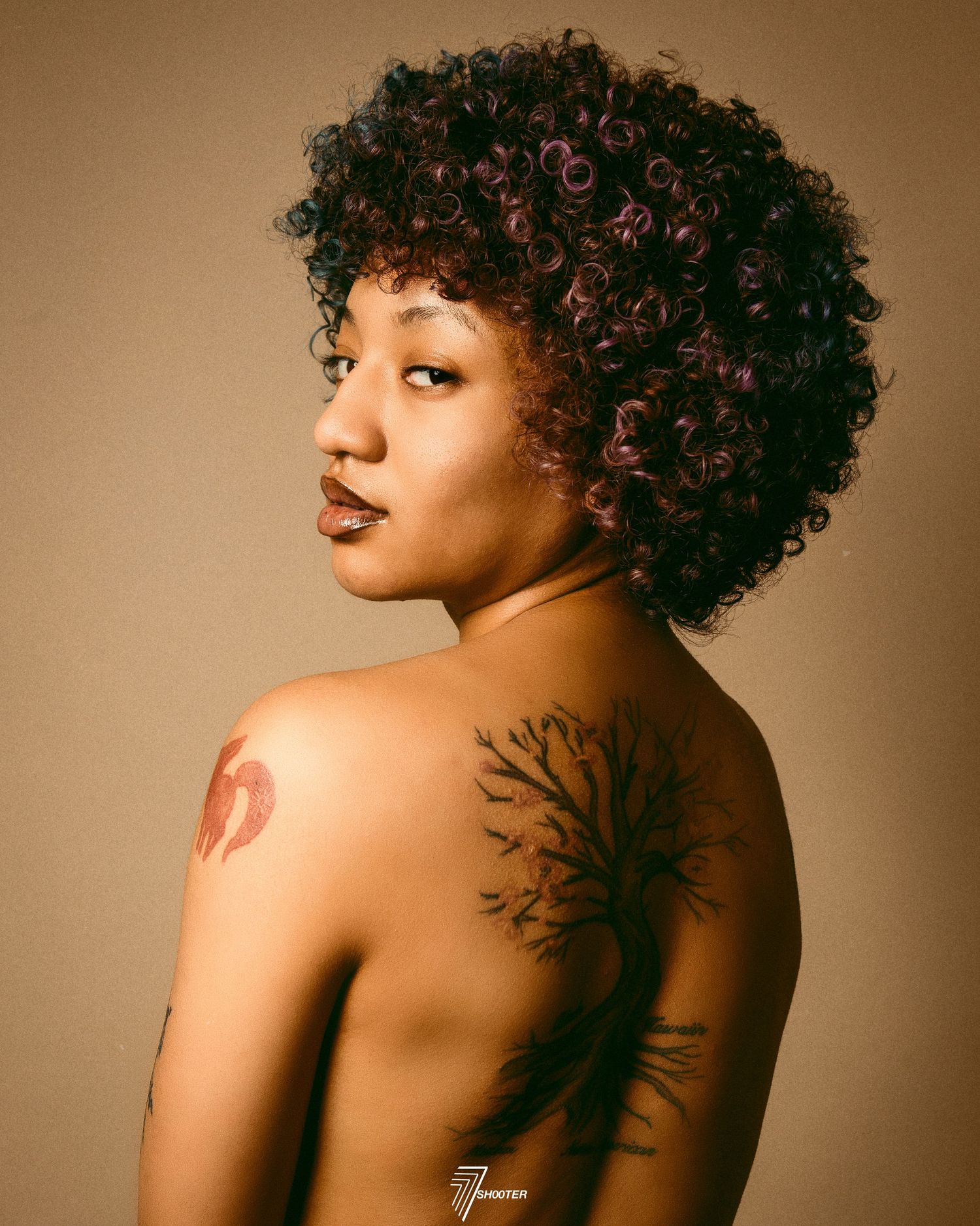 A striking artistic portrait showcasing natural curly hair and a delicate tree tattoo on bare shoulder.