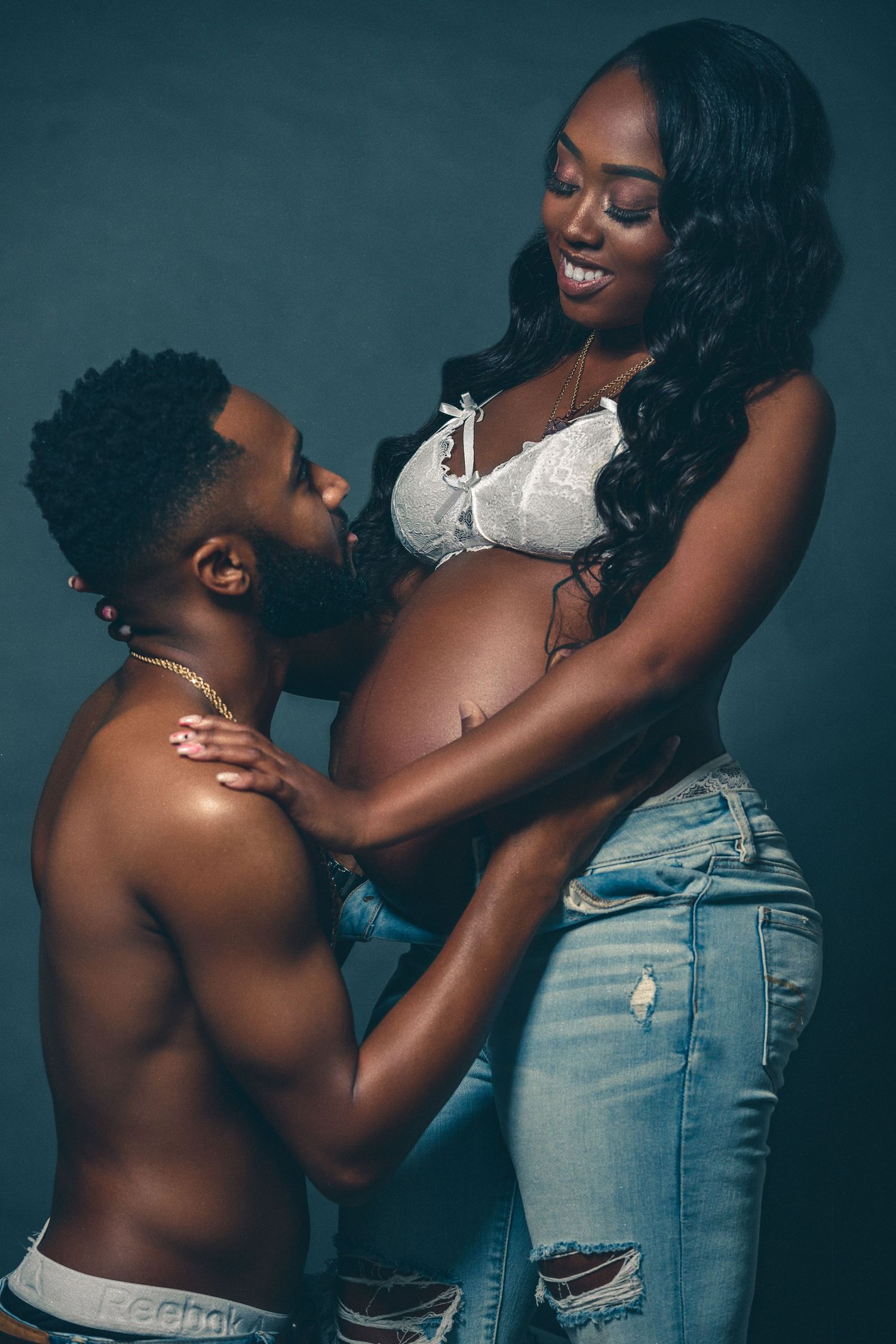 Intimate maternity photo showing couple in casual denim and white attire.