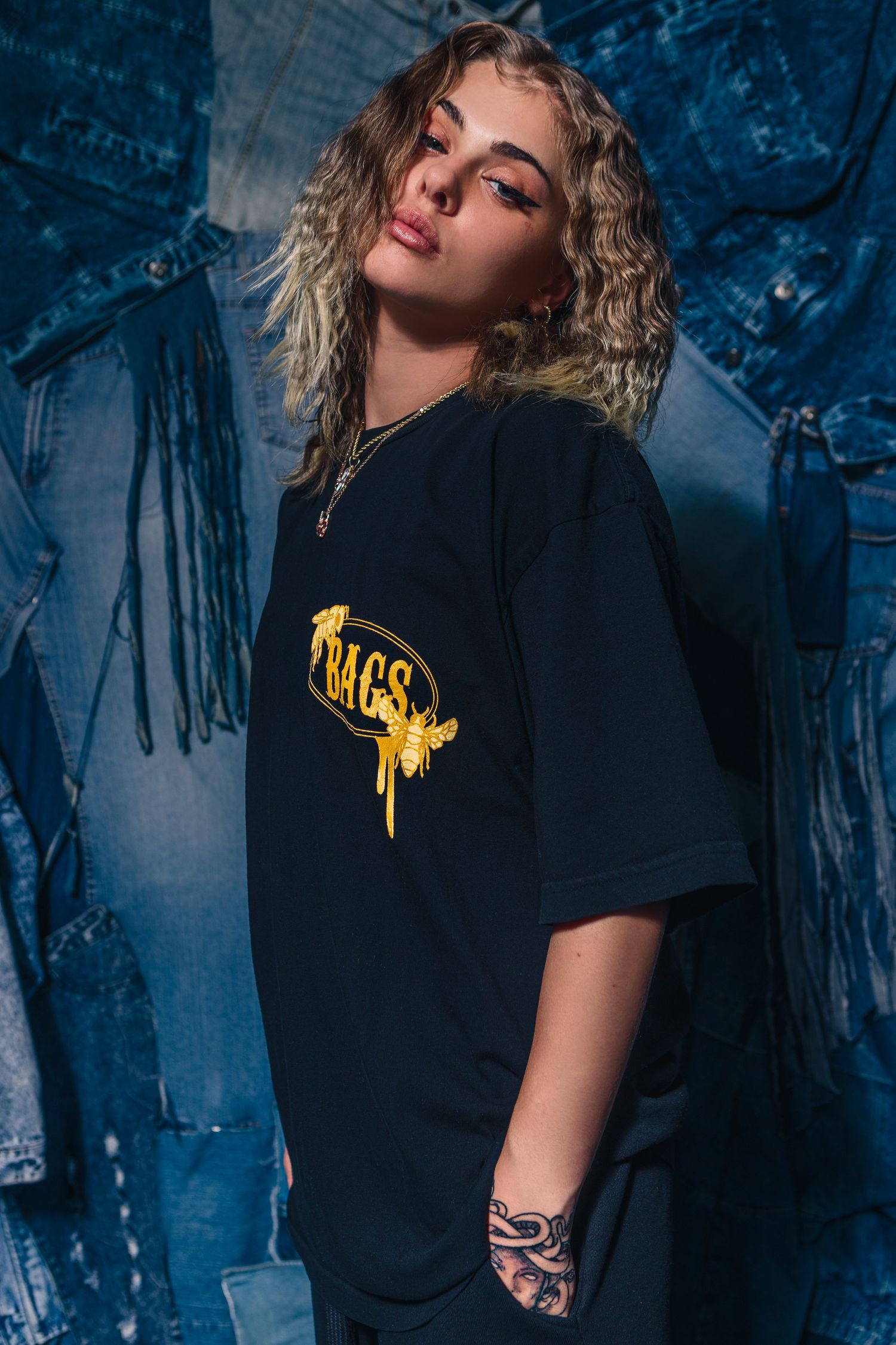 Model in black t-shirt with yellow graphic against blue textured background.