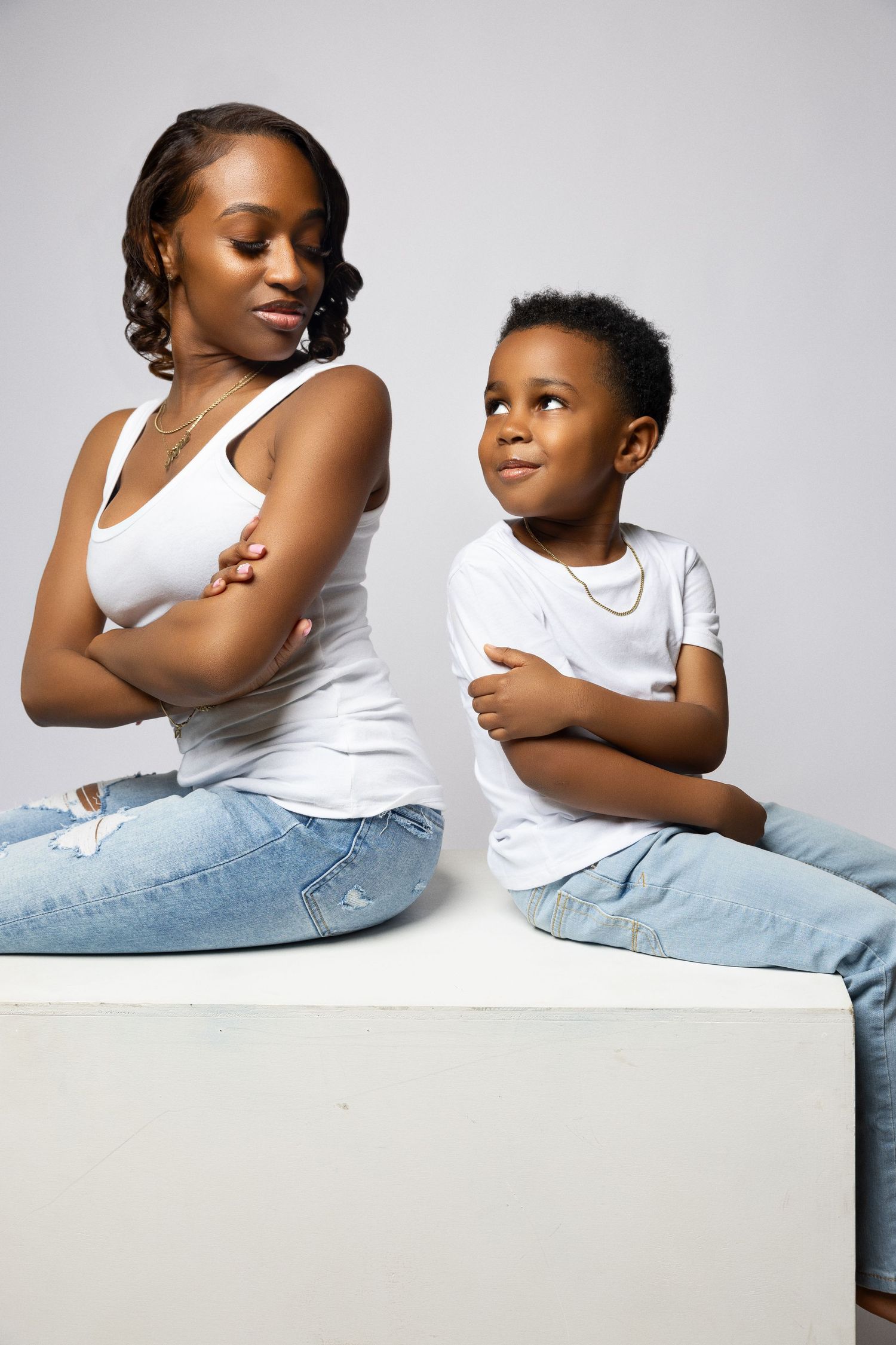A parent and child sit together in matching white tops and jeans, posing with crossed arms and playful expressions.