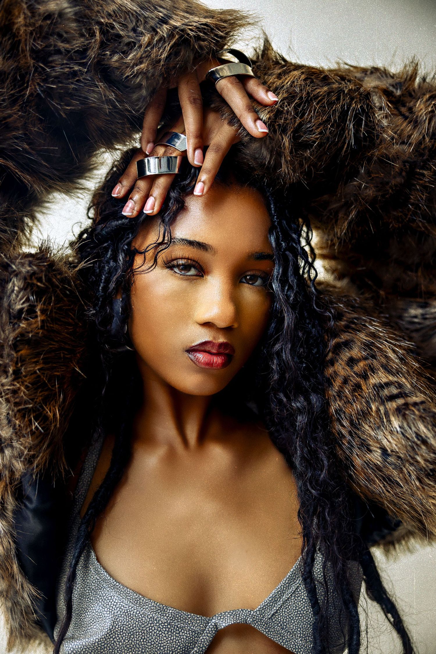 Fashion portrait with dramatic fur backdrop, glittering silver top, dark wavy hair and glamorous makeup styling.