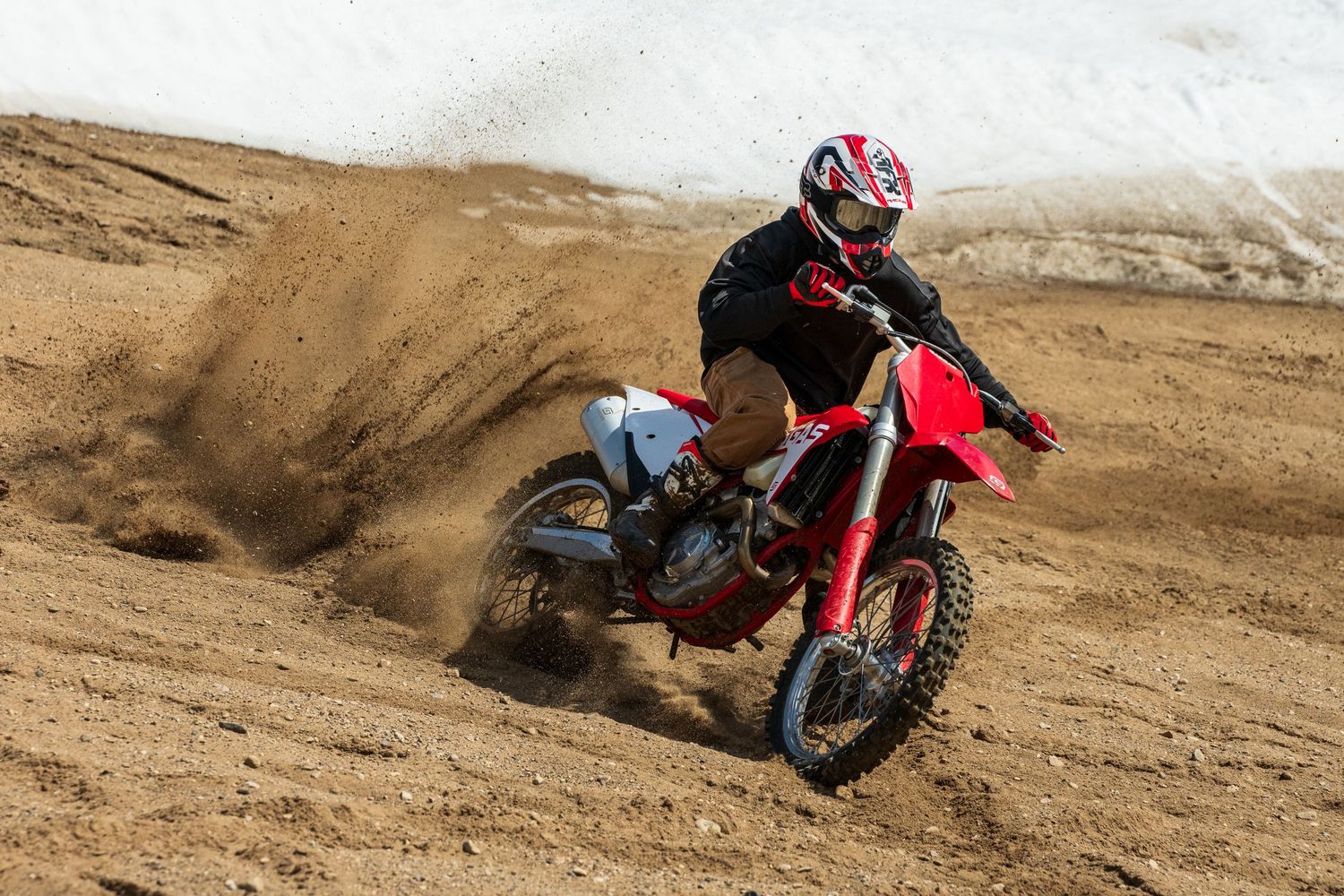 Dirt bike rider making sharp turn in sandy terrain spraying dirt.