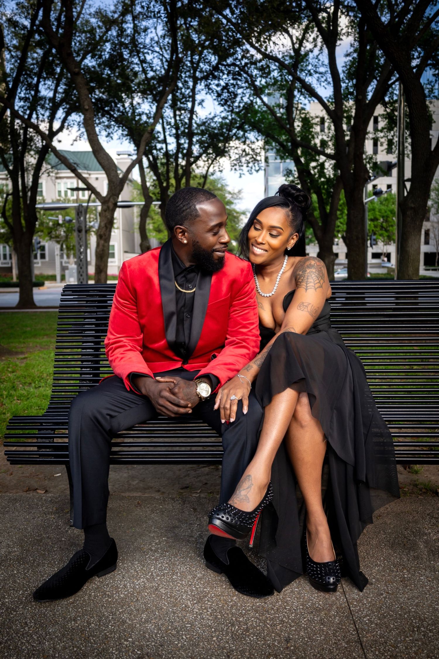 Couple in elegant evening wear sitting together on park bench surrounded by trees.