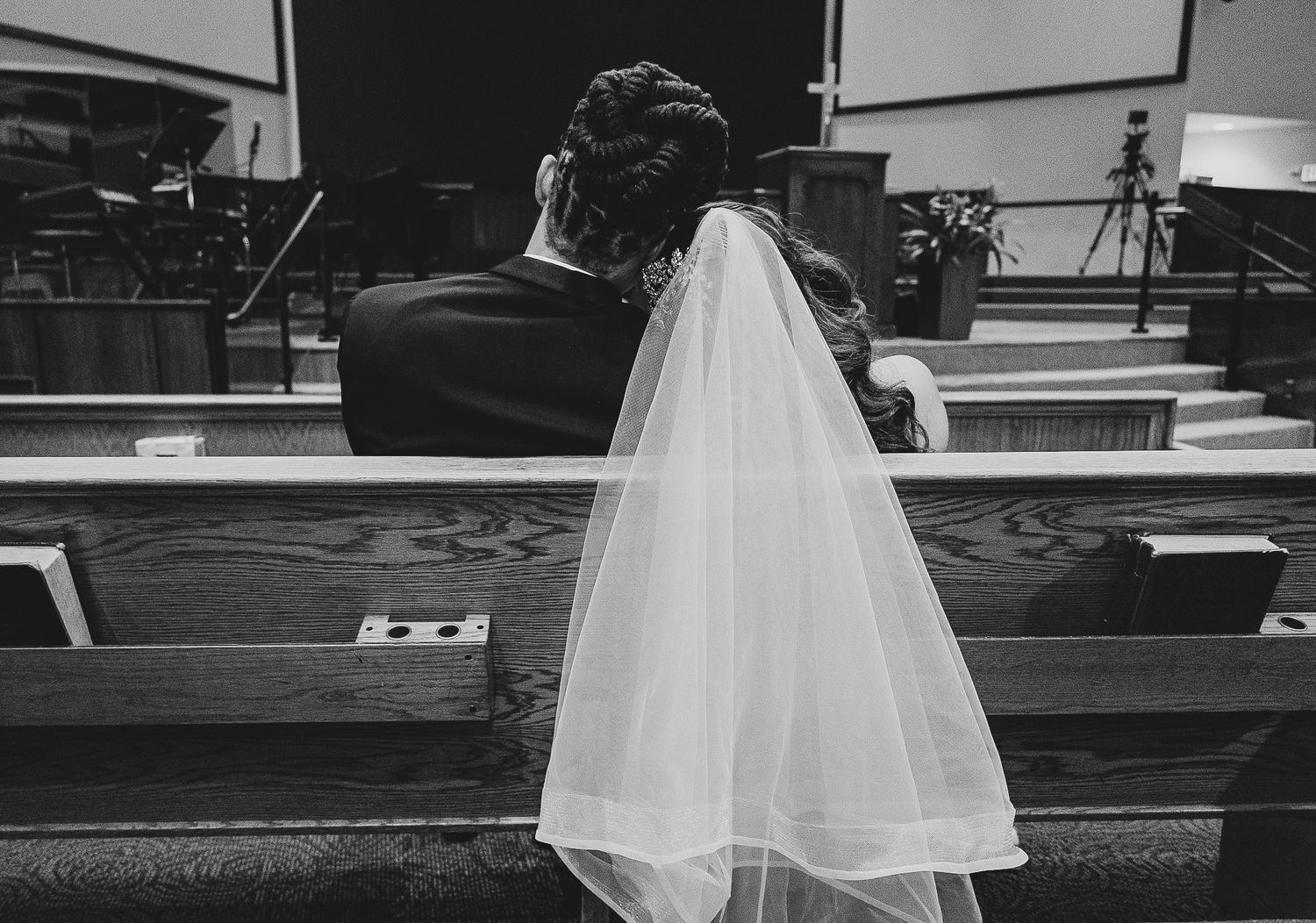 Black and white photo showing back view of couple sitting in church pew.