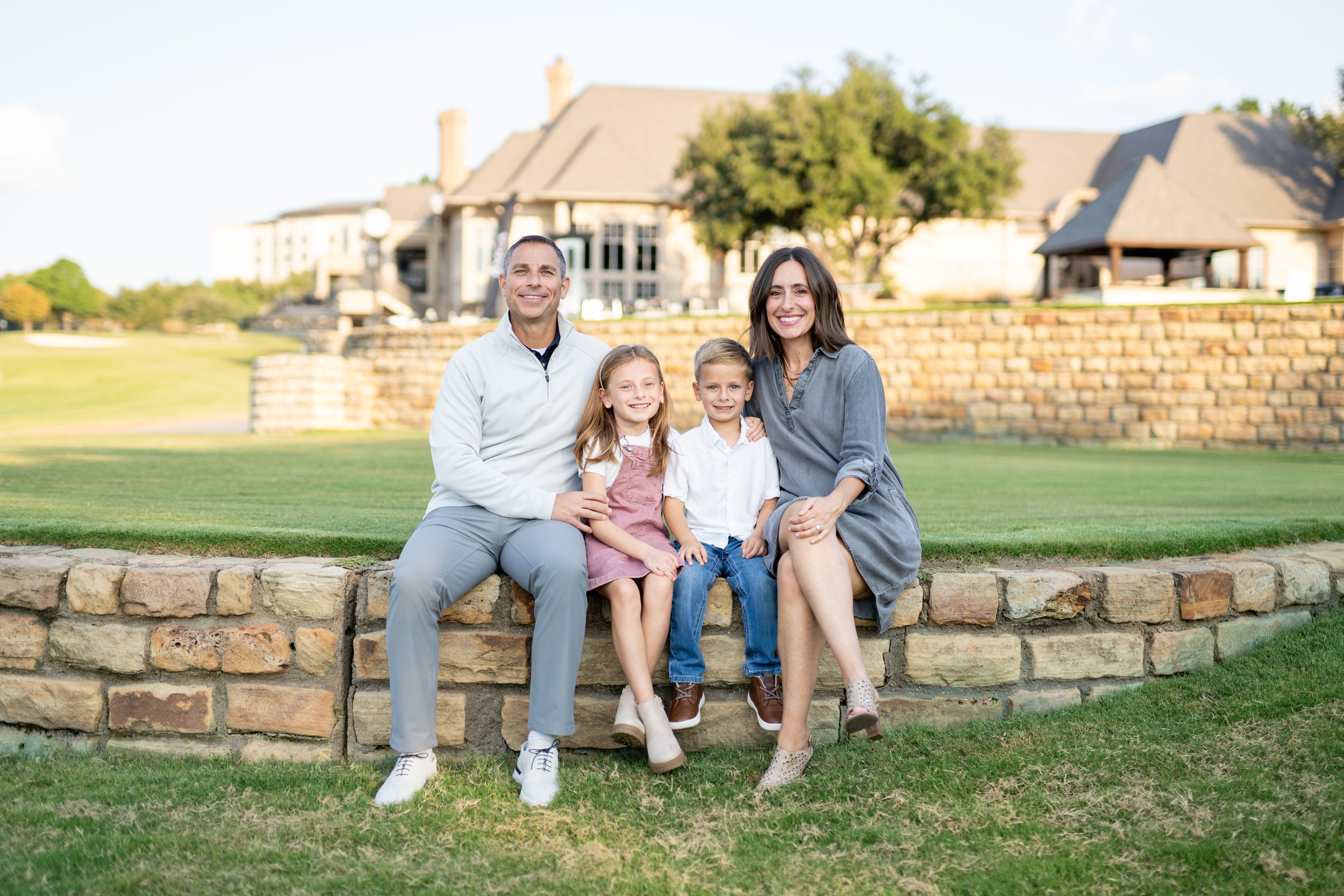 A family sits together on a stone wall with a beautiful golf course and residential homes in the background.