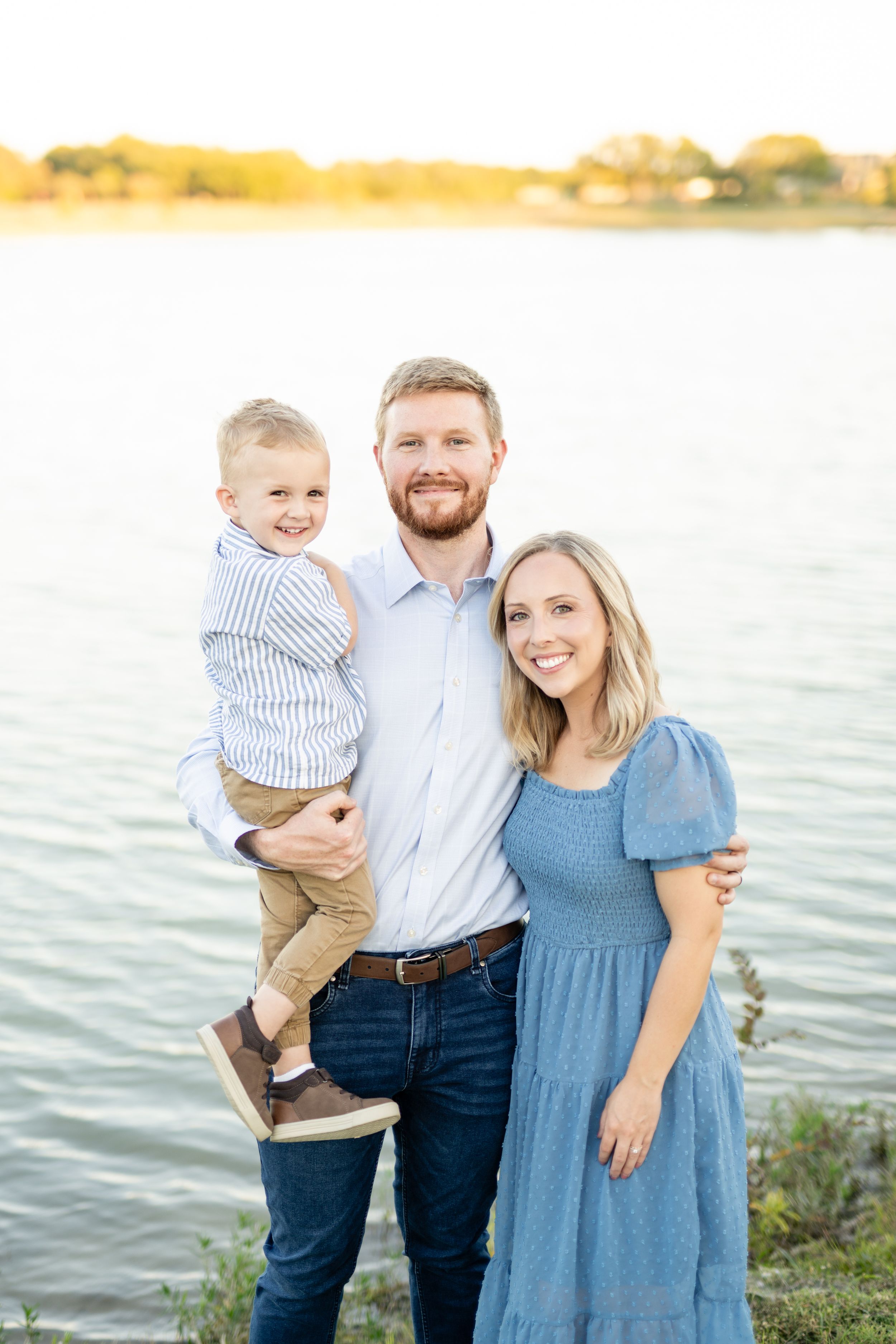 A family enjoys a sunset moment together by a calm lake on a warm evening.