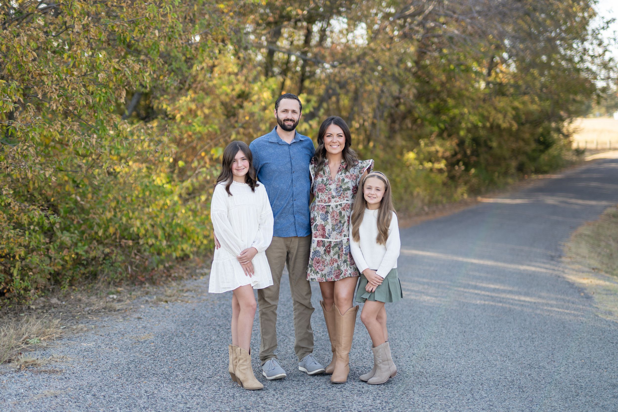 Happy family stands together on a gravel path surrounded by autumn foliage on a sunny afternoon.