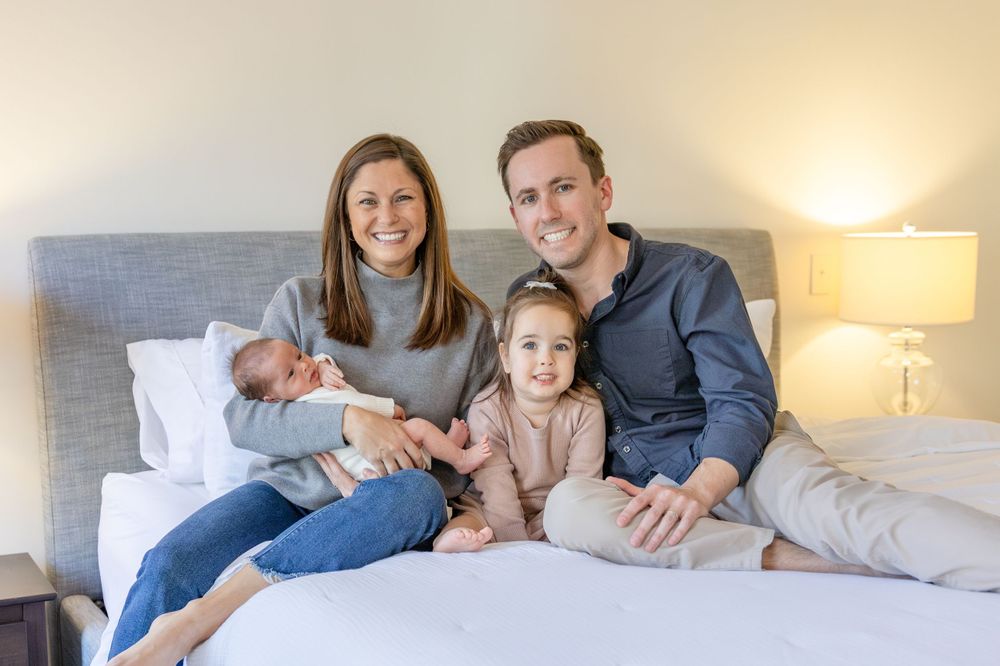 A family sits together on a bed with their baby at an at home Raleigh newborn session.