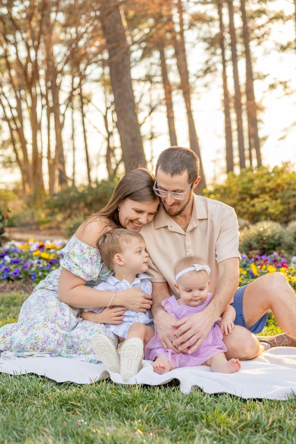 Family on a blanket in a garden with colorful flowers and pine trees at sunset at the WRAL Azalea Gardens in Raleigh by Jessie Peloso Photo