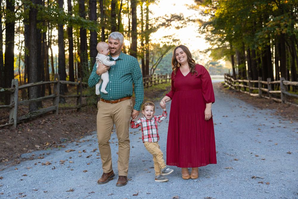 A family in coordinated fall outfits stands together on a tree-lined path during golden hour sunset by Jessie Peloso Photography.
