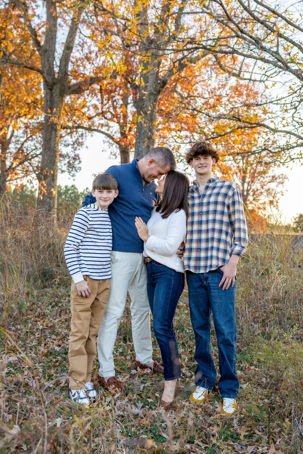 A family group poses playfully in front of autumn trees with golden leaves during a fall photo session at the NC Museum of Art.