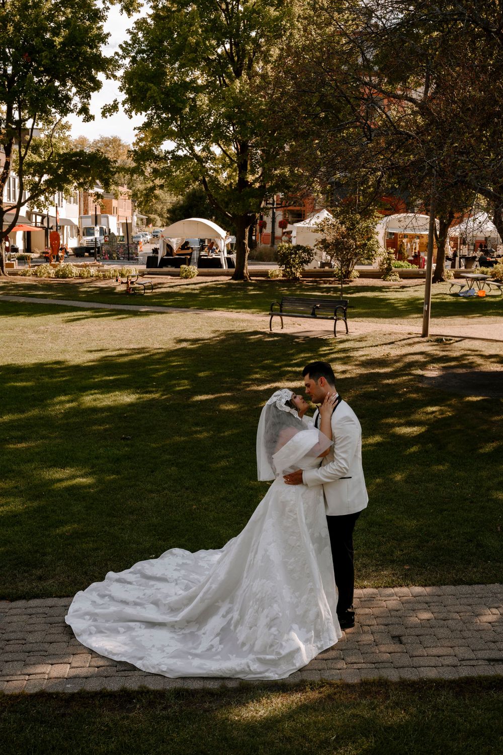 A romantic outdoor wedding ceremony in a park with white tents and lush trees in the background.