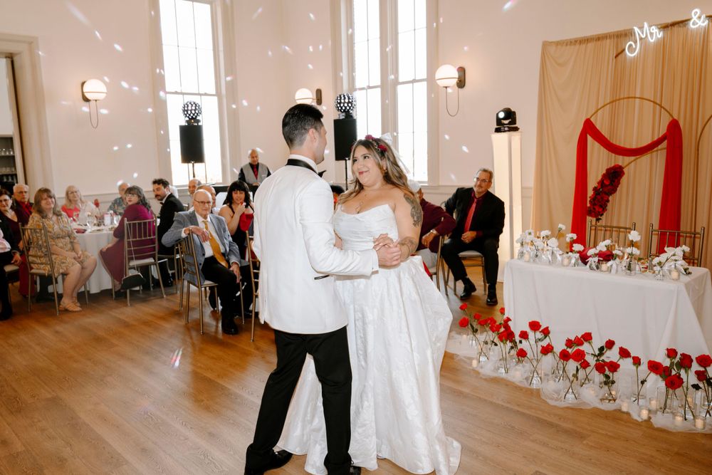 Newlyweds share an intimate dance moment in a venue decorated with string lights and red accents.