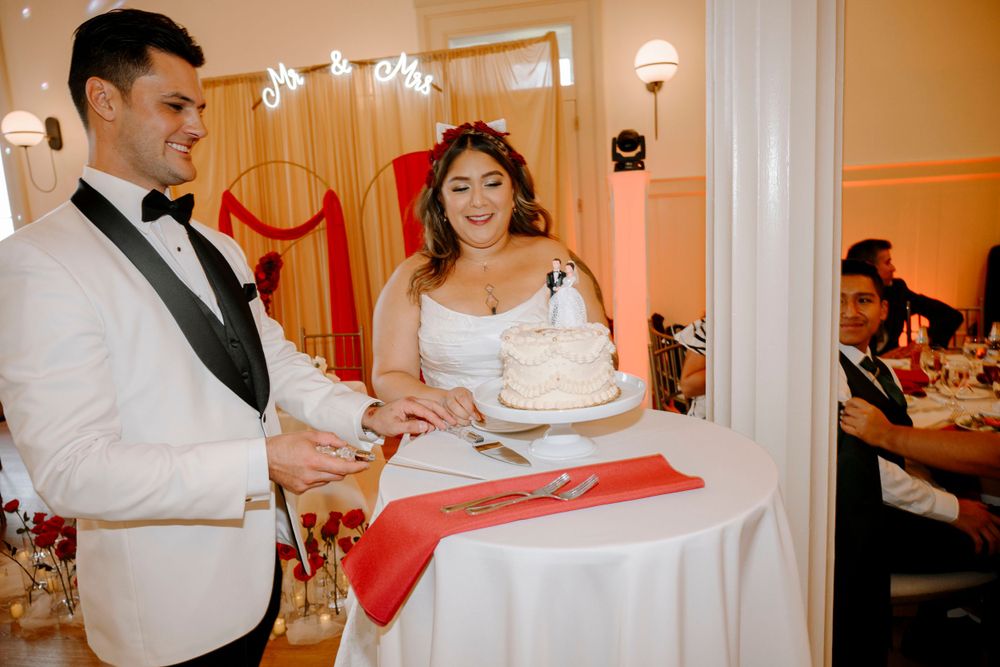 A couple cuts their wedding cake together at their reception with red decor details.