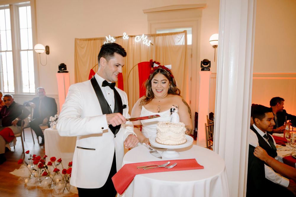 Newlyweds cut their wedding cake together at an elegant indoor reception venue with pink lighting accents.