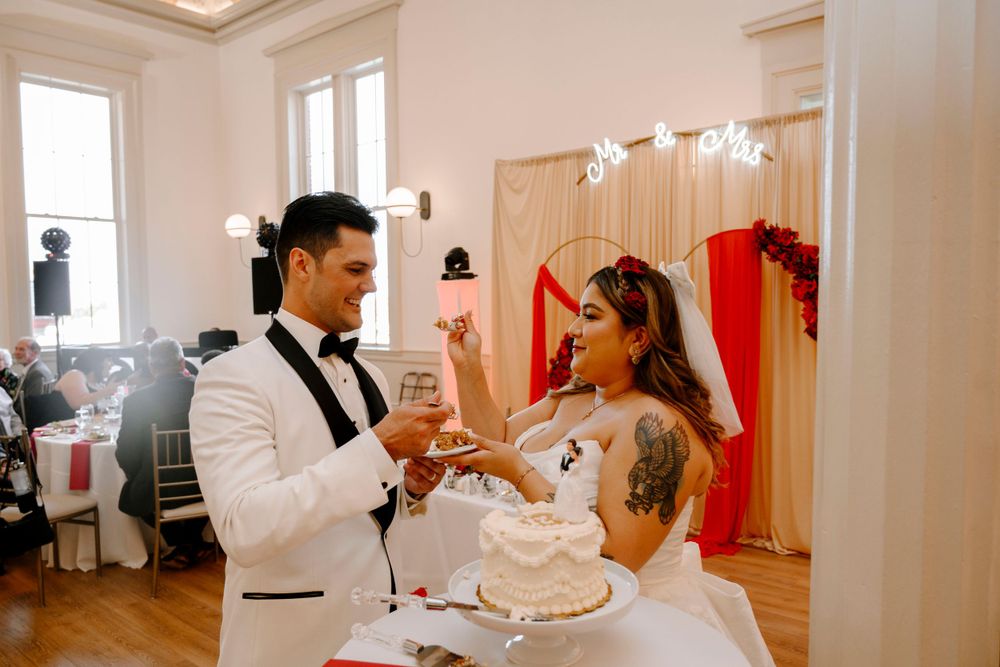 A couple cuts their white wedding cake together during their reception in an elegant indoor venue.