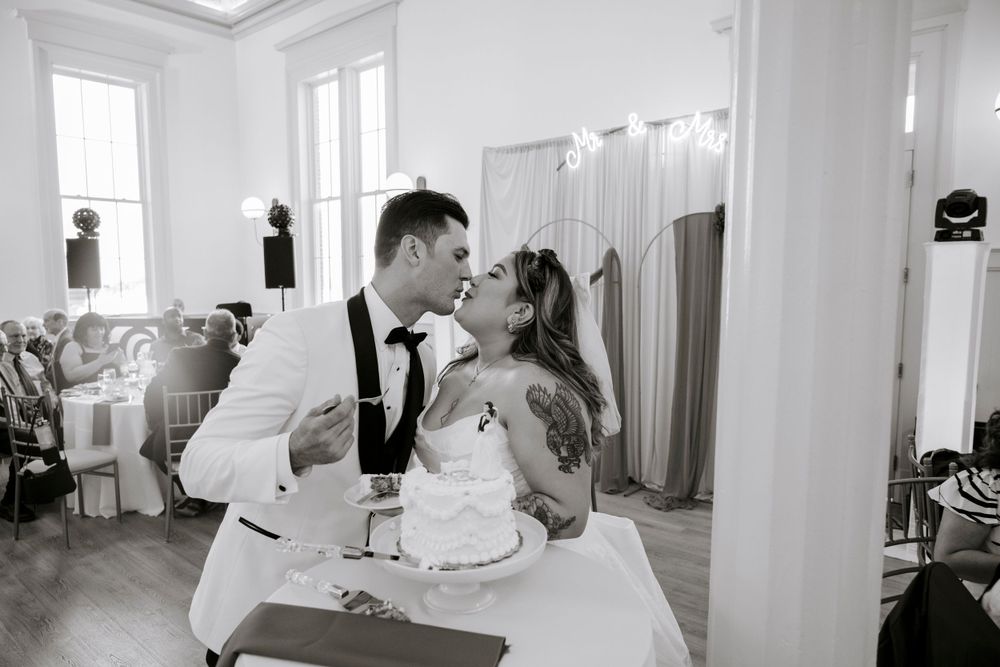 A romantic black and white moment between newlyweds sharing a kiss at their wedding reception while cutting the cake.