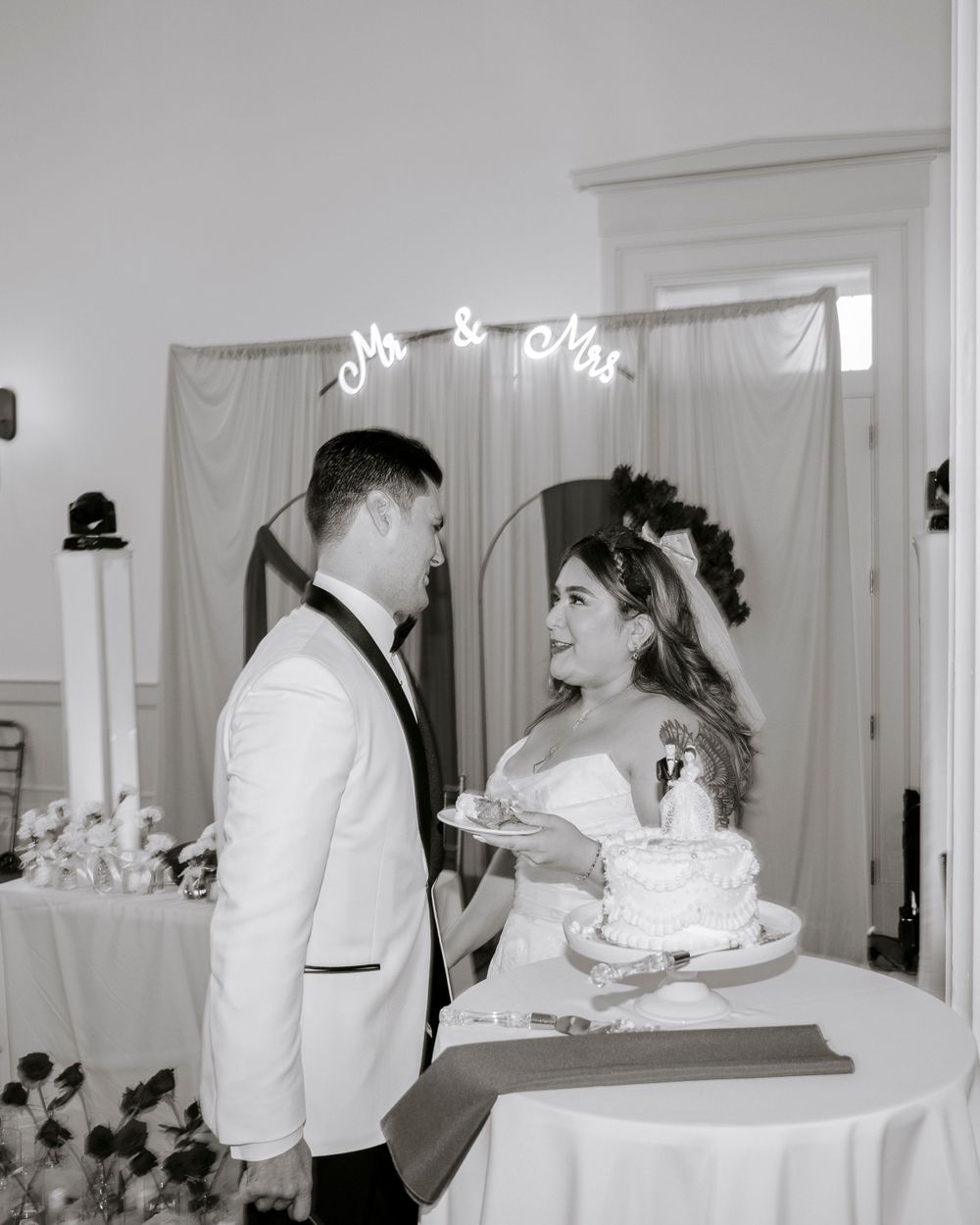 Wedding couple shares a special moment with their cake under a 'Mr & Mrs' sign at their reception.