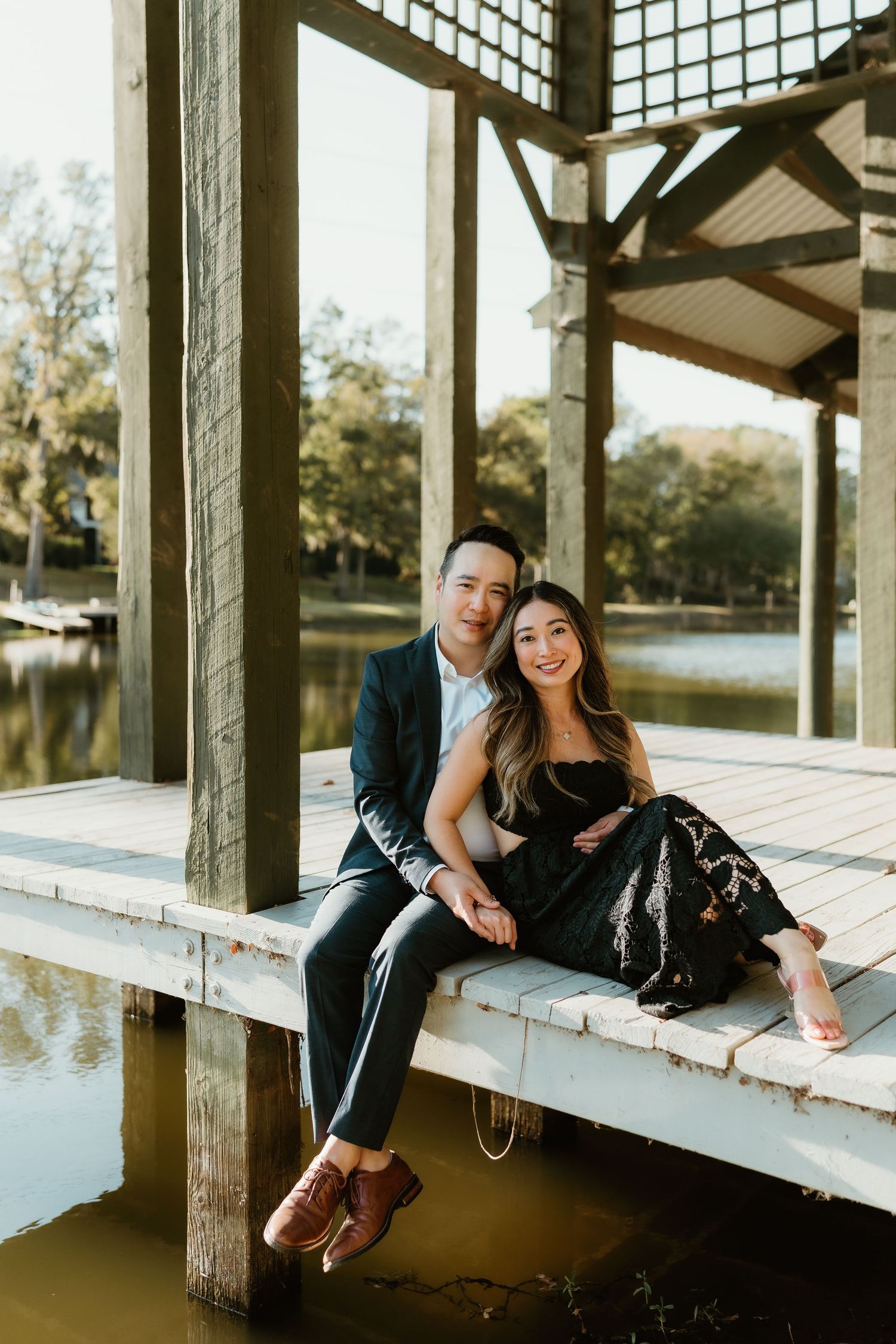 Romantic couple relaxes on wooden deck overlooking lake during sunset.