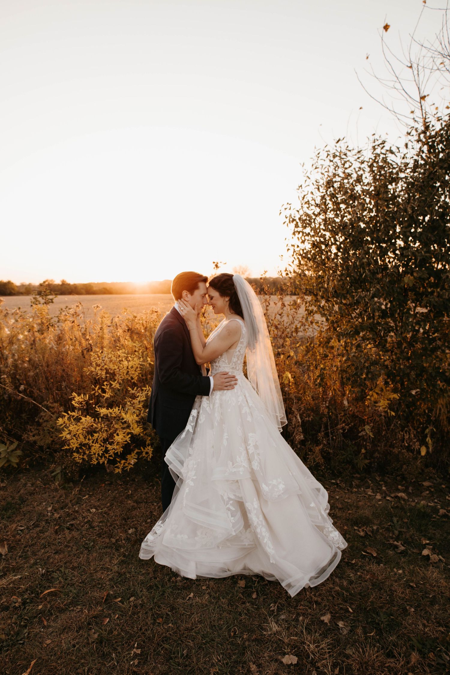 Bride and groom sharing an intimate moment in a sunlit autumn field during golden hour.