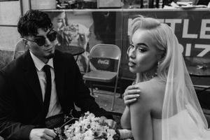 Black and white photo of stylish bride and groom sitting together at an urban cafe setting.