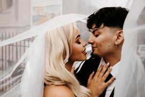 Bride and groom share an intimate moment under a flowing white veil on their wedding day.